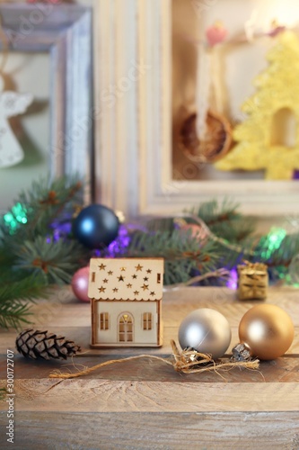 Christmas toy house, balls, cones, branches of spruce, illumination on a wooden surface, home comfort, seasonal winter holidays