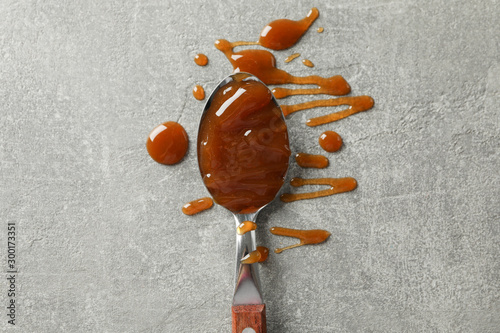 Spoon with caramel on grey background, space for text photo