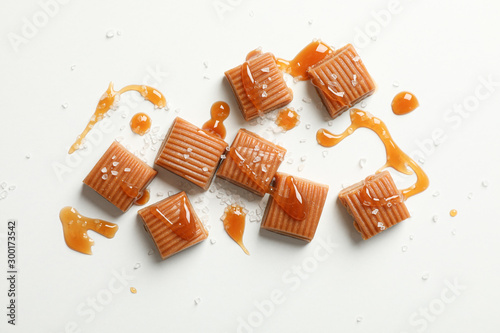 Salted caramel candies and sauce on white background, space for text