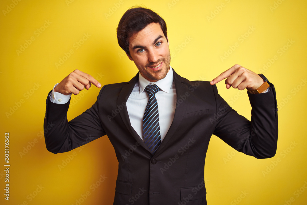 Young handsome businessman wearing suit and tie standing over isolated yellow background looking confident with smile on face, pointing oneself with fingers proud and happy. Young handsome businessman wearing suit and tie standing over isolated yellow background looking confident with smile on face, pointing oneself with fingers proud and happy.