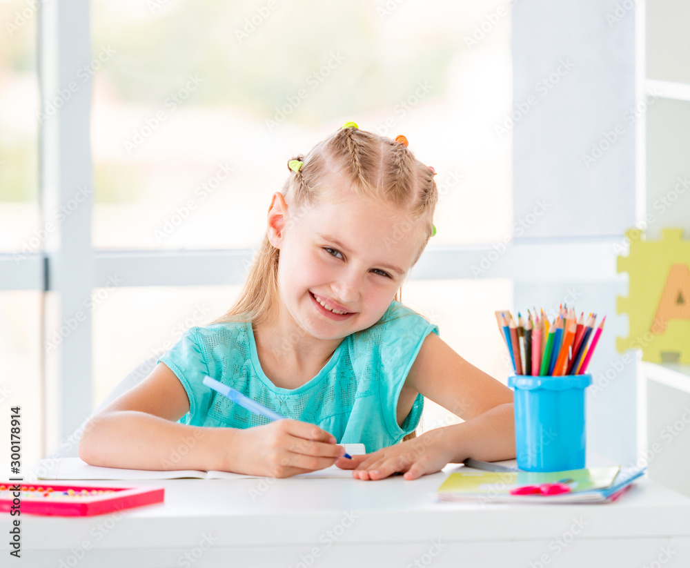 Cute kid girl sitting at the desk, coloring with pencils Cute kid girl sitting at the desk, coloring with pencils