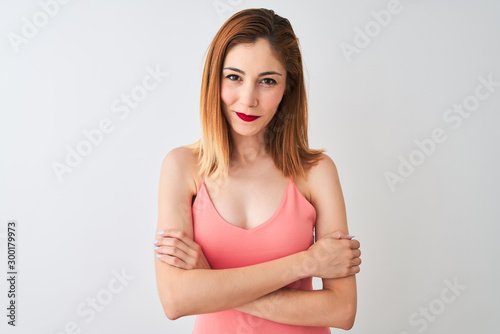 Beautiful redhead woman wearing casual pink t-shirt standing over isolated white background happy face smiling with crossed arms looking at the camera. Positive person.