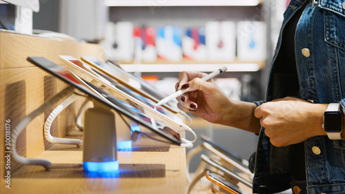 Young unrecognizable woman chooses a tablet in an electronics store, close-up. She trying using it with stylus. photo