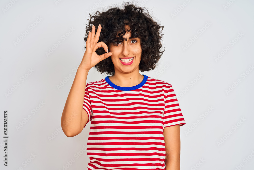 Young arab woman with curly hair wearing striped t-shirt over isolated white background smiling positive doing ok sign with hand and fingers. Successful expression. Young arab woman with curly hair wearing striped t-shirt over isolated white background smiling positive doing ok sign with hand and fingers. Successful expression.