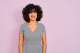 Young arab woman with curly hair wearing striped dress over isolated pink background with a happy and cool smile on face. Lucky person.