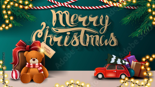 Merry Christmas, green greeting postcard with garlands, red vintage car and present with Teddy bear near the wall