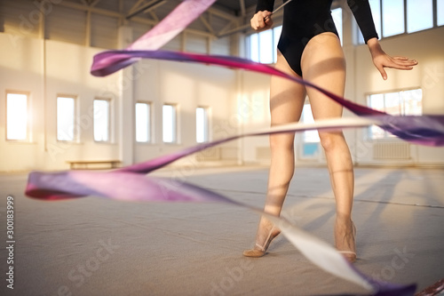 Close view of long legs of professional young gymnast training with violet ribbon in gymnstics school, active lifestyle concept