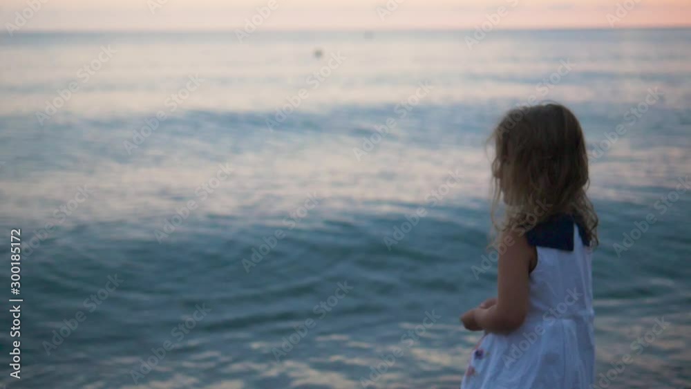 Little girl standing by the sea Close-up slow motion shot/video of a little girl/child/kid/baby standing on the pebble beach by the sea/ocean Little girl standing by the sea Close-up slow motion shot/video of a little girl/child/kid/baby standing on the pebble beach by the sea/ocean