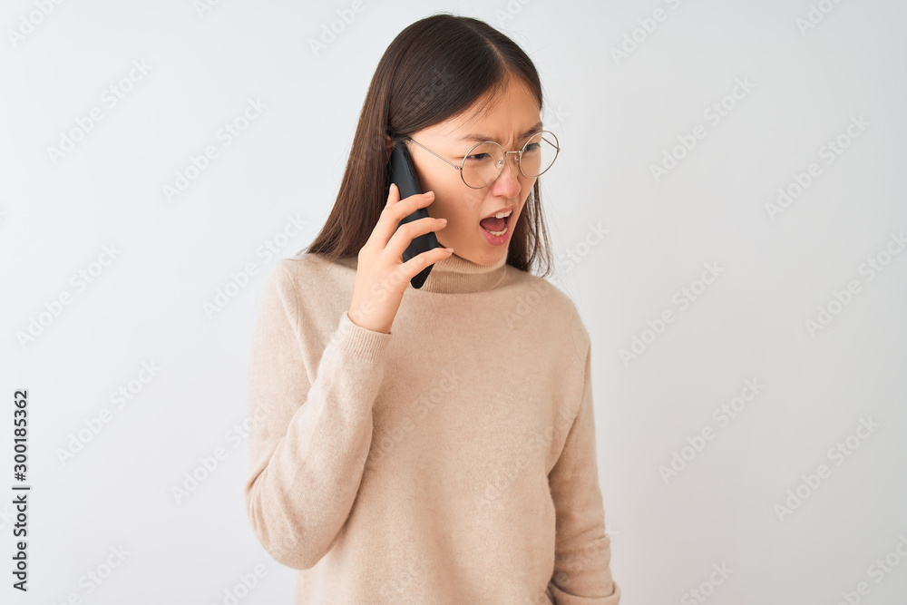 Young chinese woman talking on the smartphone over isolated white background angry and mad screaming frustrated and furious, shouting with anger. Rage and aggressive concept. Young chinese woman talking on the smartphone over isolated white background angry and mad screaming frustrated and furious, shouting with anger. Rage and aggressive concept.