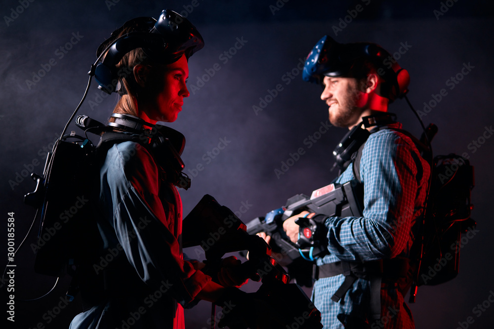 Young couple or friends stand and look in opposite sides, ready to fight. Virtual reality games, concept. Smoky background