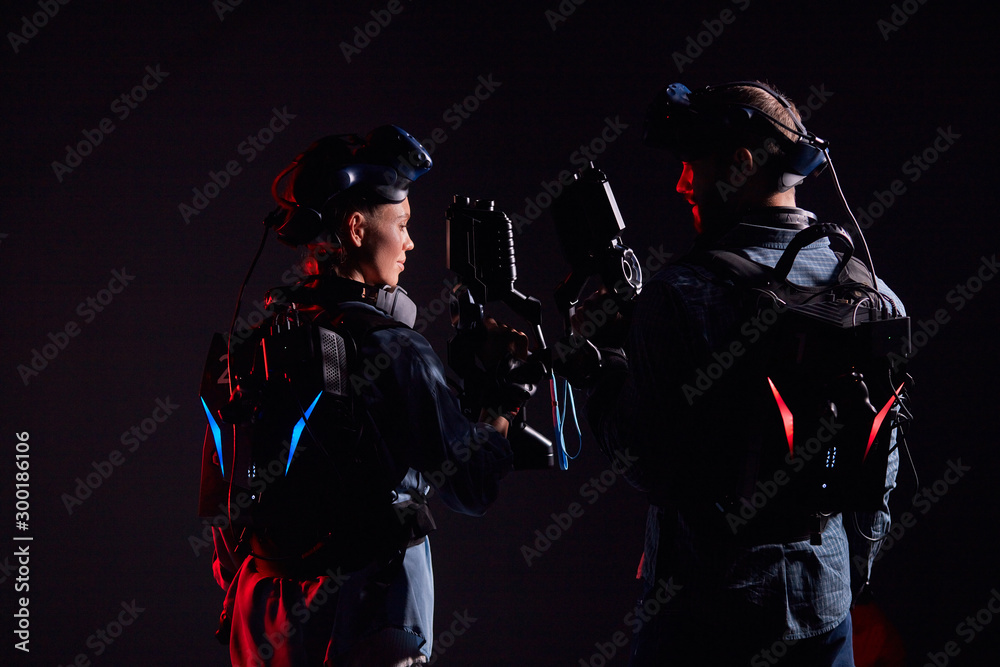 Man and woman stand opposite each other, holding vr weapons, team in virtual reality game. Isolated over black background