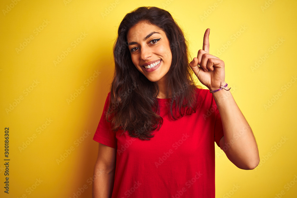 Young beautiful woman wearing red t-shirt standing over isolated yellow background surprised with an idea or question pointing finger with happy face, number one Young beautiful woman wearing red t-shirt standing over isolated yellow background surprised with an idea or question pointing finger with happy face, number one