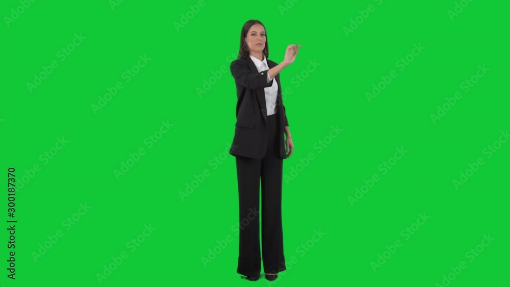 Young elegant business woman in suit interacting with virtual reality touch screen. Full length on green screen background. Young elegant business woman in suit interacting with virtual reality touch screen. Full length on green screen background.