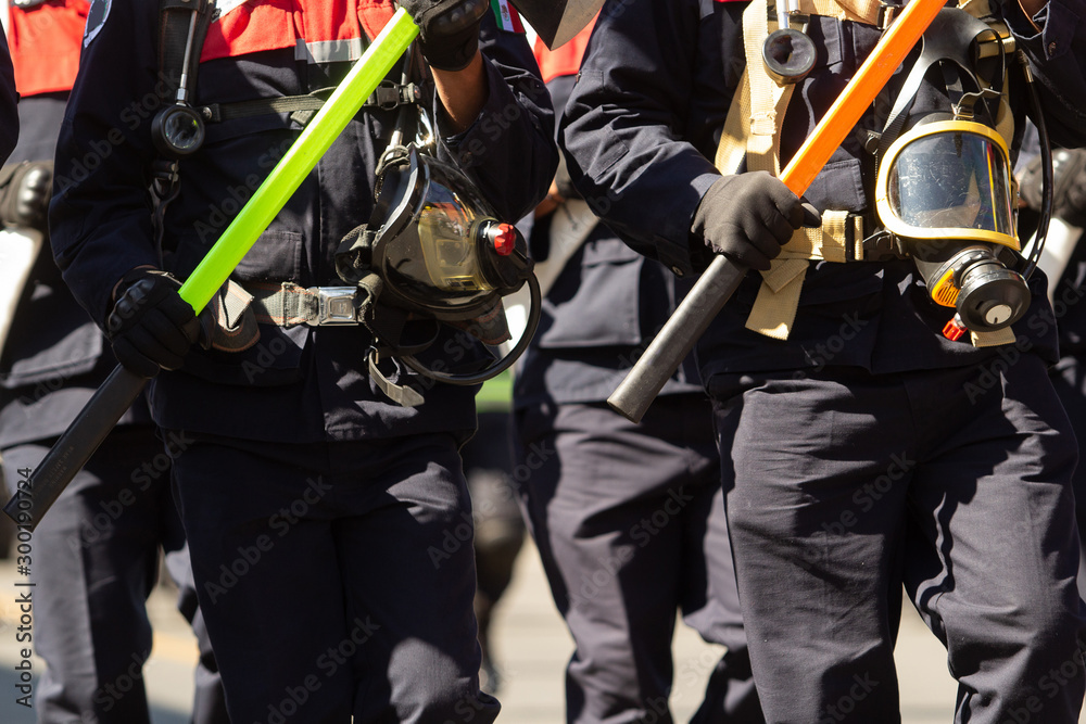 a group of firemen walking in a parade holding in their hands axes and special fireman equipment, blue firemen suits a group of firemen walking in a parade holding in their hands axes and special fireman equipment, blue firemen suits