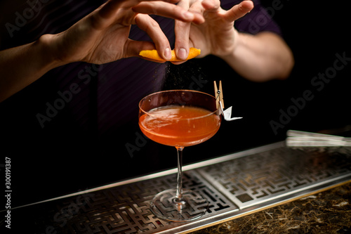 Professional bartender spraying on the cocktail decorated with paper airplane in the clothespin with a orange zest juice