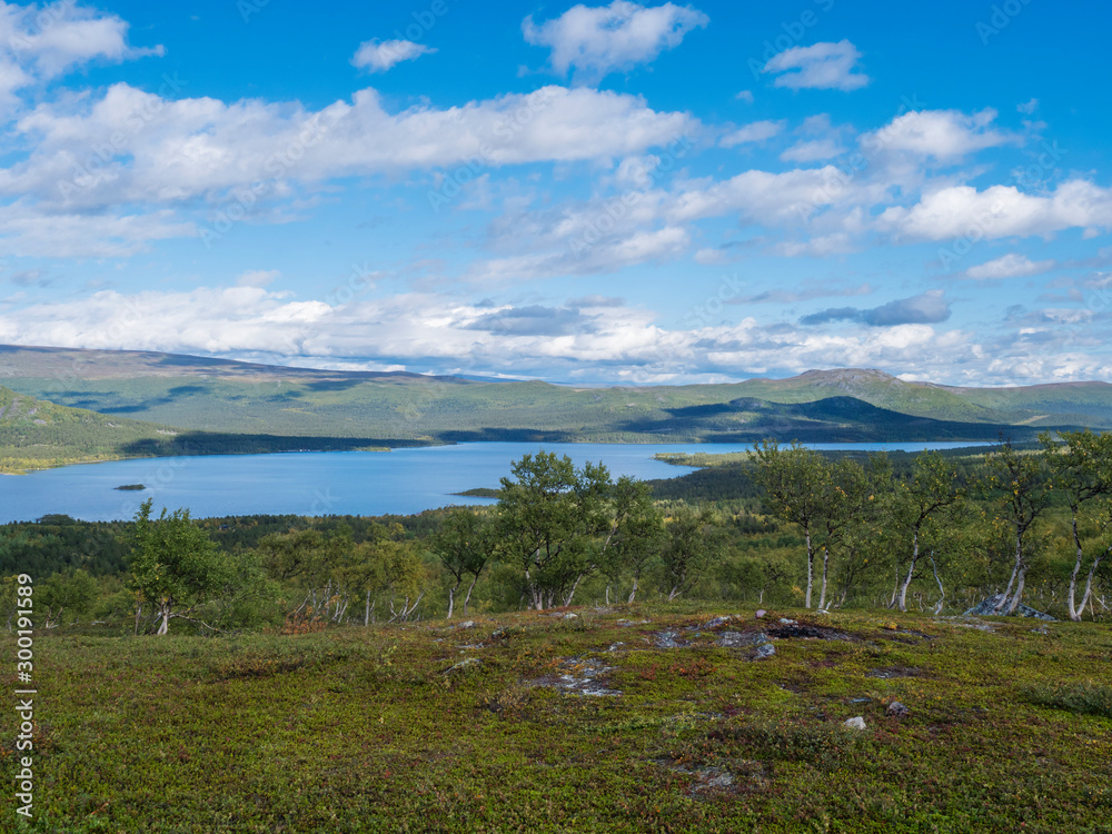 Lapland landscape with beautiful river Lulealven, snow capped mountain, birch tree and footpath of Kungsleden hiking trail near Saltoluokta, north of Sweden wild nature. Summer blue sky