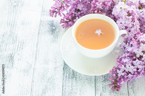 Cup of herbal tea and lilac on wooden background. Rays of sunlight - Image