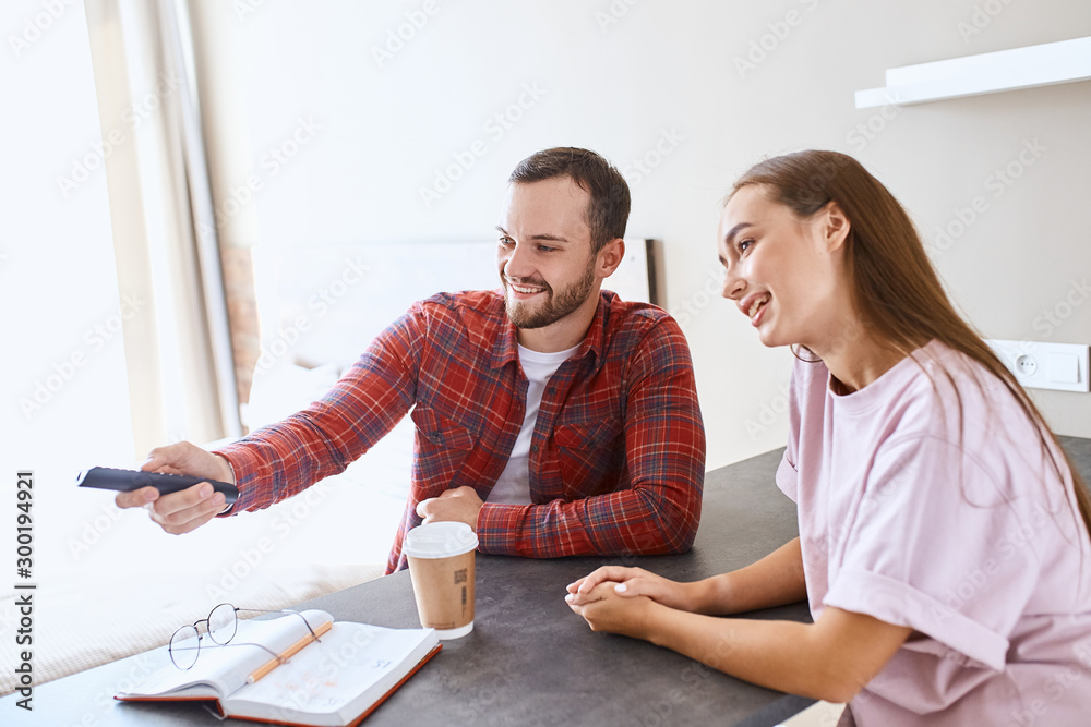 Pleasant nice husband and wife sitting at table in hotel room, watching tv, chatting lovely, choosing good film, indoor shot, portrait Pleasant nice husband and wife sitting at table in hotel room, watching tv, chatting lovely, choosing good film, indoor shot, portrait