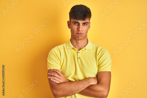 Young indian man wearing casual polo standing over isolated yellow background skeptic and nervous, disapproving expression on face with crossed arms. Negative person.