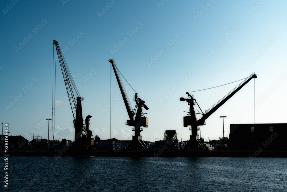 silhouette of port cranes in a large commercial port under a blue evening sky at twilight