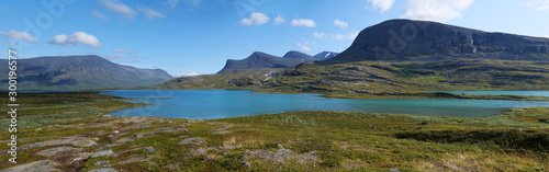 Lapland nature landscape wide panorama of blue glacial lake Allesjok near Alesjaure, birch tree forest, snow capped mountains. Northern Sweden, at Kungsleden hiking trail. Summer sunny day