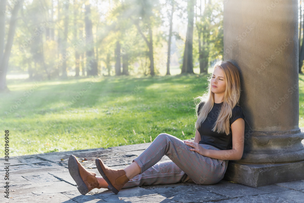 Attractive young girl is sitting with closed eyes in the rays of autumn sun in the park. Attractive young girl is sitting with closed eyes in the rays of autumn sun in the park.