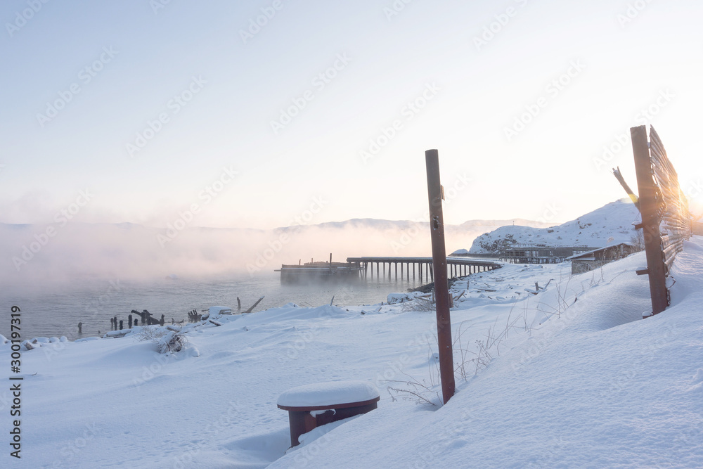 old wooden pier for large ships on the river bank covered in thick white fog from the water at dawn on a frosty winter day outside the Arctic Circle old wooden pier for large ships on the river bank covered in thick white fog from the water at dawn on a frosty winter day outside the Arctic Circle
