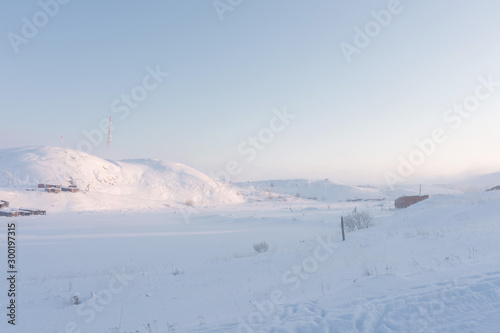 a valley covered with deep white snow and hills with high television radio towers on a hill on a frosty winter day in the far north © Александр Коновалов