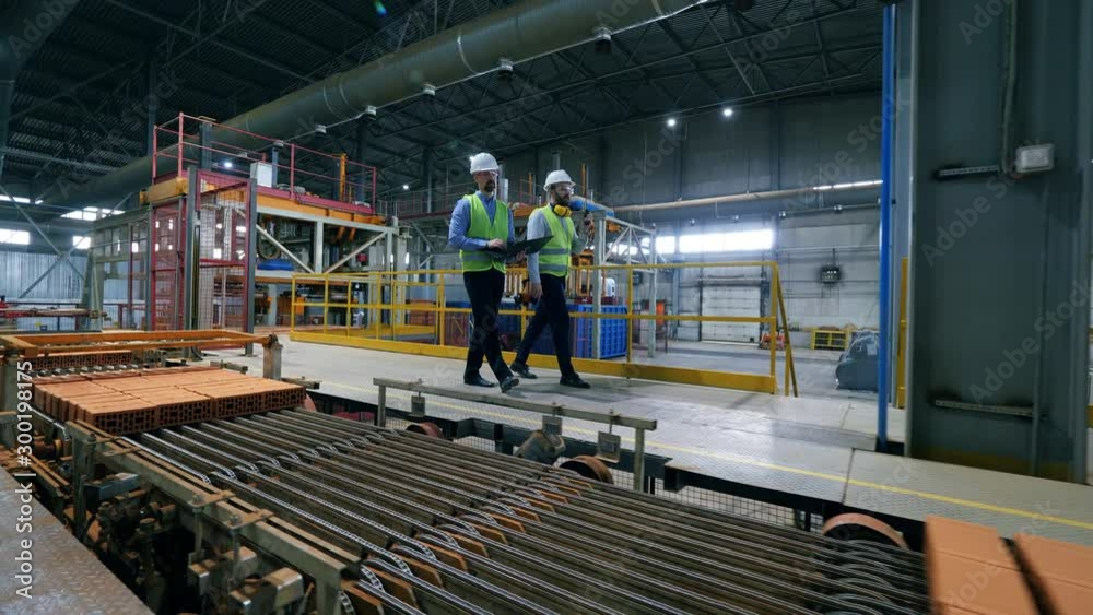 Male engineers walk at a modern industrial plant, checking pallets with bricks. Male engineers walk at a modern industrial plant, checking pallets with bricks.