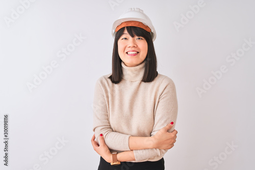 Young beautiful Chinese architect woman wearing helmet over isolated white background happy face smiling with crossed arms looking at the camera. Positive person. © Krakenimages.com