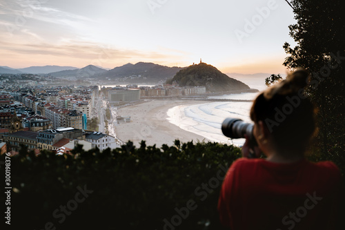Young tourist girl taking a photo of San Sebastian from Mount Ulia during sunset photo