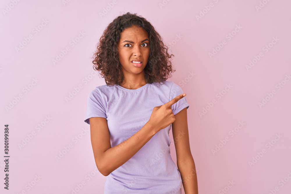 Young brazilian woman wearing t-shirt standing over isolated pink background Pointing aside worried and nervous with forefinger, concerned and surprised expression Young brazilian woman wearing t-shirt standing over isolated pink background Pointing aside worried and nervous with forefinger, concerned and surprised expression