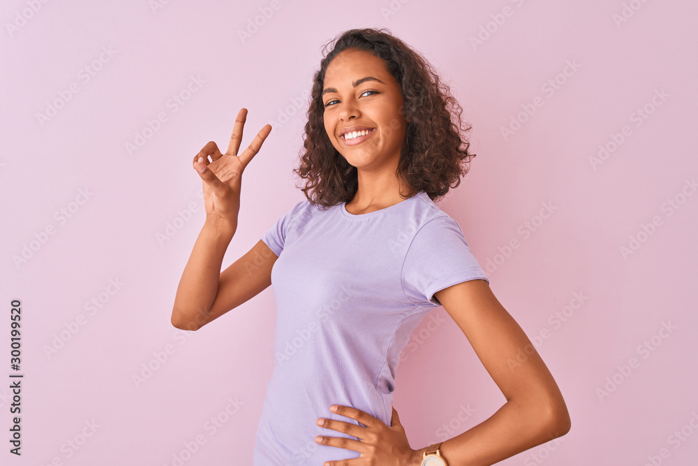 Young brazilian woman wearing t-shirt standing over isolated pink background smiling looking to the camera showing fingers doing victory sign. Number two. Young brazilian woman wearing t-shirt standing over isolated pink background smiling looking to the camera showing fingers doing victory sign. Number two.