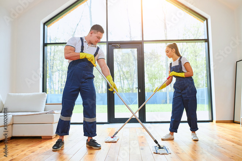 Effective job mopping wooden floor in apartment, two caucasians in blue uniform with mop for washing floor