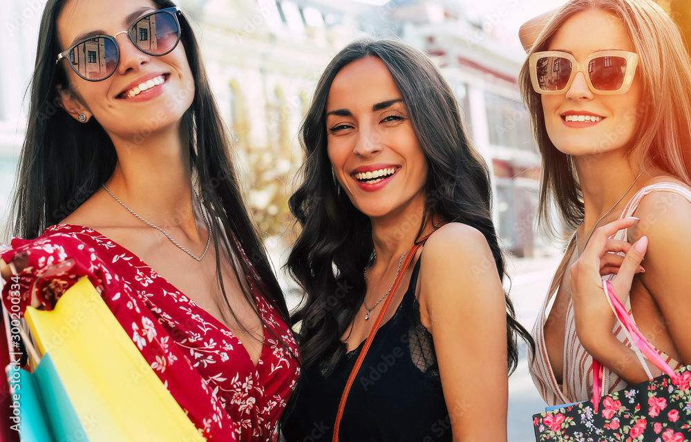 Glamorous life. Close up photo of three young adult women in sunglasses and summer outfits, smiling happily after the shopping in the town.
