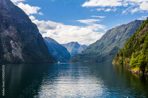 Scenic landscape View on the mountain peaks with green slopes and surface of water and feather clouds on the sky on background in sunny day. Neroyfjord - the narrowest fjord in Norway, Gudvangen Flam photo