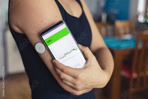 Woman checking glucose level with a modern technology remote sensor and mobile phone, without blood. Diabetes treatment. photo