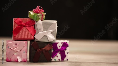 Gift boxes on table with decorative lights on black background with a gift rolling into the video frame