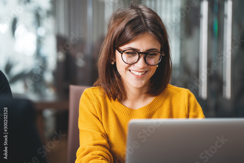 Portrait of happy business woman wearing glasses at workplace in office. Young handsome female worker using modern laptop photo
