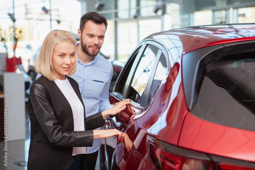 Happy couple examining new automobile at car dealership, copy space. Beautiful woman and her husband choosing new auto to buy
