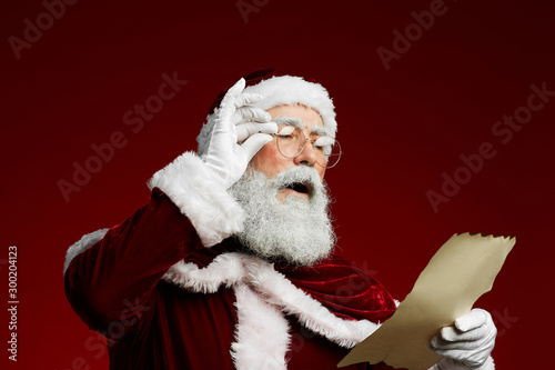 Obraz na plátne Waist up portrait of classic Santa reading list on parchment standing against re