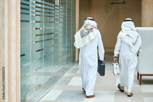 Photos Rear view on sheikh businessmen holding case of money, going to meeting negotiations