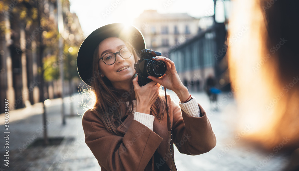 Photographer in glasses with retro camera take photo girlfriend. Tourist smiling girl in hat travels in Barcelona holiday with friend. Sun flare street in europe city. Traveler hipster shoot girls