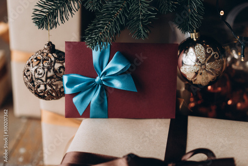 Gift voucher in burgundy envelope with blue bow under the Christmas tree. Christmas gift