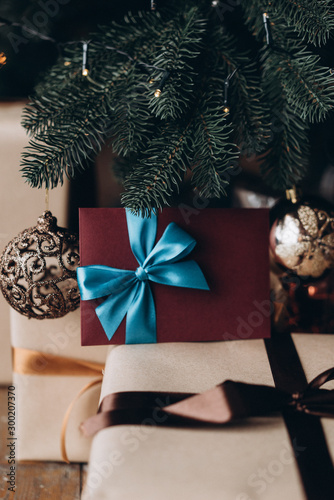 Gift voucher in burgundy envelope with blue bow under the Christmas tree. Christmas gift