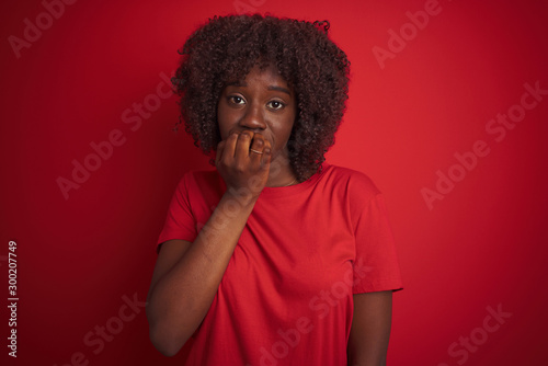 Young african afro woman wearing t-shirt standing over isolated red background looking stressed and nervous with hands on mouth biting nails. Anxiety problem. © Krakenimages.com