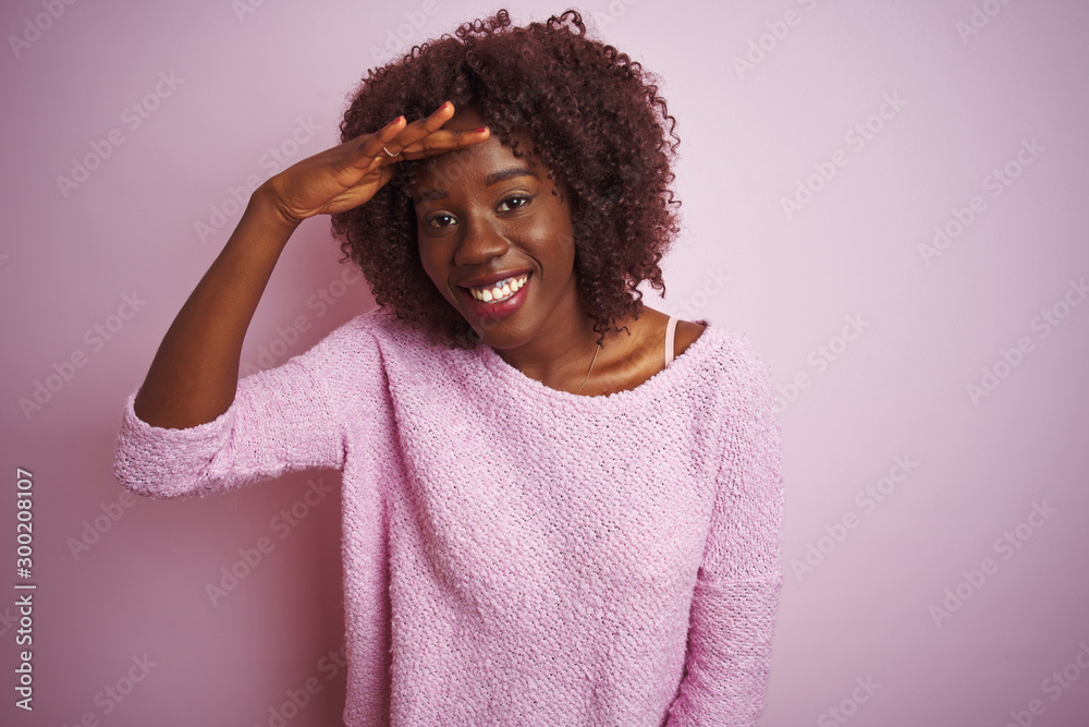 Young african afro woman wearing sweater standing over isolated pink background very happy and smiling looking far away with hand over head. Searching concept. Young african afro woman wearing sweater standing over isolated pink background very happy and smiling looking far away with hand over head. Searching concept.