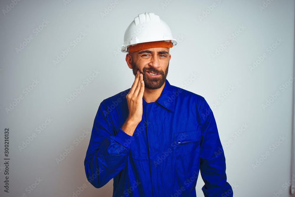 Handsome indian worker man wearing uniform and helmet over isolated white background touching mouth with hand with painful expression because of toothache or dental illness on teeth. Dentist concept. Handsome indian worker man wearing uniform and helmet over isolated white background touching mouth with hand with painful expression because of toothache or dental illness on teeth. Dentist concept.