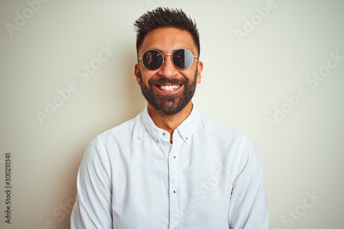 Handsome indian buinessman wearing shirt and sunglasses over isolated white background with a happy and cool smile on face. Lucky person.