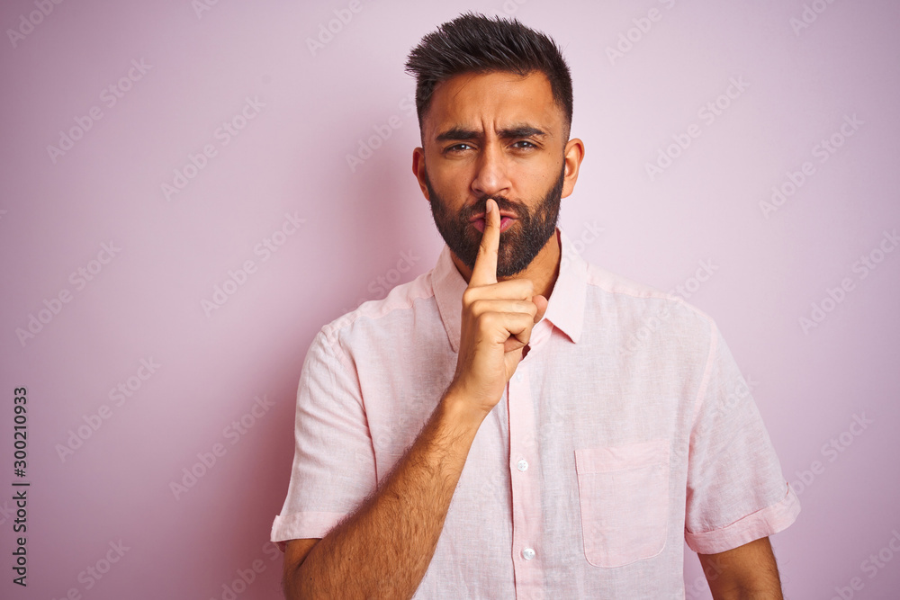Young indian man wearing casual shirt standing over isolated pink background asking to be quiet with finger on lips. Silence and secret concept. Young indian man wearing casual shirt standing over isolated pink background asking to be quiet with finger on lips. Silence and secret concept.